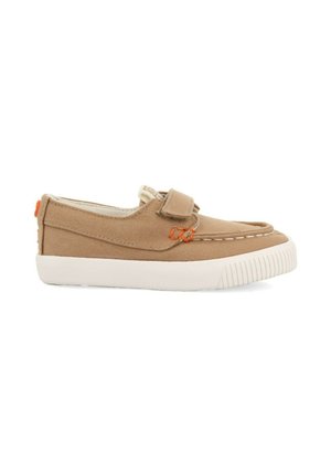 Zapatillas de lona en color beige con suela de goma blanca, que presentan un cierre con tira, detalles de costura y un logotipo naranja en la parte trasera.