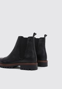 Black leather Chelsea boots featuring a textured finish, elastic side panels, a pull tab, and a brown leather welt on a rugged sole.