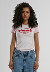 Short-sleeve T-shirt with a pink collar and white body, featuring a red graphic logo. Paired with blue high-waisted jeans.