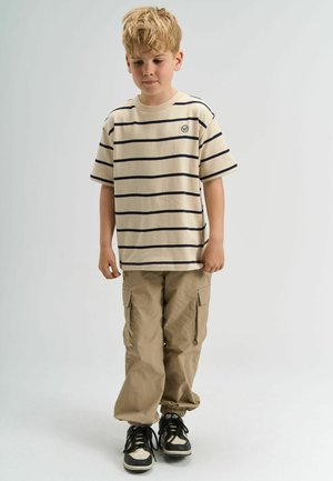 Beež triibuline T-särk tumesiniste joontega, lühikeste varrukatega ja logoga; sobitatud heleda beeži cargo-pükstega ja mustade tossudega valgete aktsentidega.