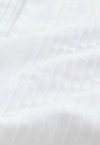 Valge kangas, millel on tekstureeritud muster vertikaalsete triipudega. Materjal näeb välja sile ja pehme, kerge ja õhulise kvaliteediga.