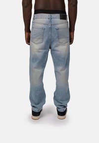 Jasnoniebieskie dżinsy o luźnym kroju, z tylkimi kieszeniami i czarnym paskiem, noszone z czarnymi trampkami.