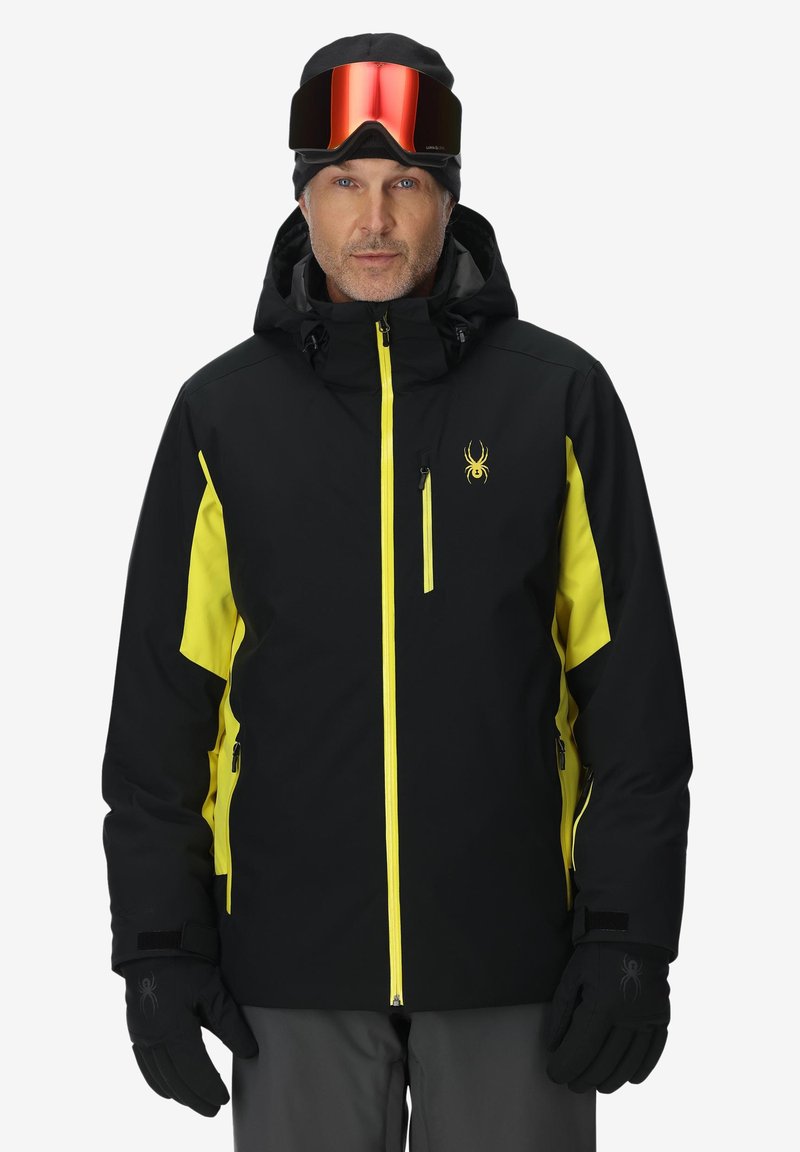 Schwarze und gelbe Skijacke mit Kapuze, Reißverschlusstaschen und Spinnenlogo. Verfügt über eine glatte Textur und kontrastierende Farben für bessere Sichtbarkeit.