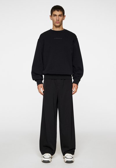 Sort sweatshirt med dropped shoulders og ribbede manchetter, parret med løse sorte bukser. Hvide sneakers fuldender looket.
