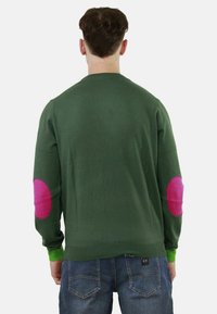 Maglione verde con maniche lunghe, caratterizzato da toppe rosa sui gomiti e dettagli verdi ai polsini. Struttura morbida, scollatura classica a girocollo.