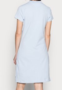 Světle modré šaty s krátkým rukávem vyrobené z měkké bavlny. Mají klasický límec a volný střih, s délkou okraje končící v polovině stehen.