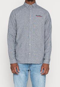 Pánská košile s dlouhým rukávem a knoflíky, v modrobílém tečkovaném vzoru, vyrobená z měkké látky, s límečkem na knoflíky a vyšitým logem.