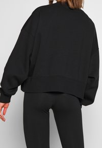 Black cropped sweatshirt with dropped shoulders and ribbed cuffs, featuring a soft, smooth texture. Worn with black leggings.