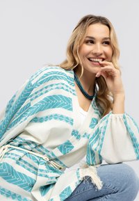 Lättvikts kimono-inspirerad kimono i vitt med turkosa geometriska mönster. Har ballongsärmar och en fransad nederkant, knuten med ett bälte.