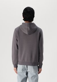Grijze hoodie van een gestructureerde stof, met een grote capuchon, geribbelde manchetten en zoom. Zicht van achteren, gecombineerd met lichtblauwe broek.