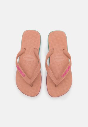 Lyserøde gummiflip-flops med teksturerede såler og teal-accenter. Har tynde stropper og "havaianas"-branding i strålende lyserød.