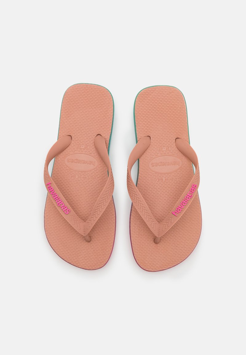 Vaaleanpunaiset kumiset flip-flopit, joissa on teksturoidut pohjat ja teal-väriä. Ominaisuuksiin kuuluvat ohuet strapsit ja "havaianas"-brändäys kirkkaan vaaleanpunaisena.