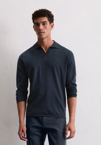 Donkerblauwe long-sleeve polo met V-hals, voorzien van een subtiel geborduurd logo op de borst en geribde manchetten. Soepele textuur.