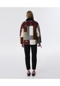 Patchwork jas met een mix van geruite, effen en gemêleerde materialen in rood, bruin, grijs en wit. Zwarte kraag en ontspannen pasvorm.