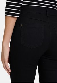 Svarta denimjeans med slim fit, bakfickor med vinklad sömnad och en slät struktur. Svart midjeband med knappdetalj.