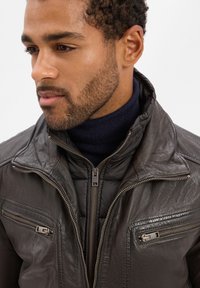 Veste en cuir gris foncé avec une doublure matelassée, dotée de poches zippées et d'un col montant. La texture est lisse avec un éclat subtil.