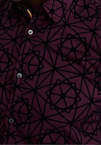 Burgundská košile s černým geometrickým vzorem, s designem na knoflíky a kontrastními černými knoflíky. Materiál se zdá být hladký a lehký.