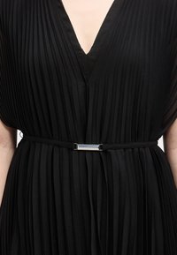 Μαύρο φόρεμα με πιέτες και στενή ζώνη με ασημένια ορθογώνια αγκράφα στη μέση και V-ντεκολτέ.