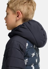 Marinblått puffjacka med huva, med ett mönstrat tyg på sidan som visar ljusa tecknade figurer. Strukturerad kviltad design.