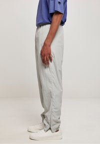 Lysegrå, løstsiddende bukser med elastik i taljen og lynlåse ved benenderne, lavet af et letvægtsmateriale. Kombineret med hvide sneakers.