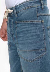 Shorts de mezclilla azul claro con cintura ajustable, que cuentan con dos bolsillos traseros y un acabado desgastado. La costura es de color contrastante y visible.