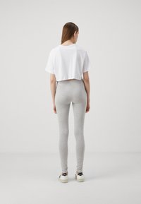 White cropped t-shirt, grey high-waisted leggings, and white sneakers with black accents. The background is a plain light color.