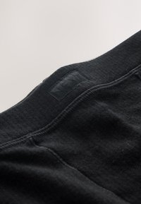 Svart bomullsunderkläder med ribbad struktur, utrustade med en platt midjeresår märkt "NEXT." Tyget verkar mjukt och elastiskt.