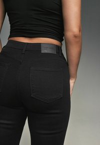 Zwarte denim high-waisted jeans met een gladde textuur, voorzien van een leren patch op de tailleband en twee achterzakken.