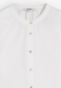 Blusa blanca de tejido suave, con un escote redondo, cierre frontal de botones metálicos y detalle fruncido en los hombros.