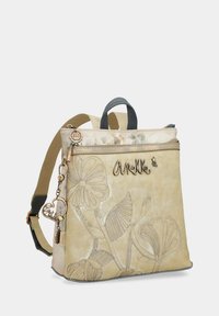 Zaino in pelle beige chiaro con rilievi floreali, manico superiore, spallacci regolabili e dettagli hardware decorativi. Chiusura con zip in cima.