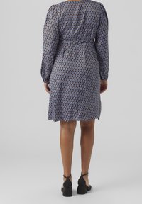 Blå mönstrad klänning med långa ärmar, åtdragen midja och en lätt utsvängd fåll. Har en upprepande bågdesign i ljusa och mörka nyanser.