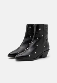 Botas de cuero negro hasta el tobillo con tacones bajos, punteras puntiagudas y tachuelas en forma de estrella plateadas decorando la superficie.