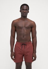 Costume de baie pentru bărbați de culoare roșie închisă, din țesătură ușoară, de lungime medie (până la coapsă), cu talie elastică și detaliu cu șnur negru.
