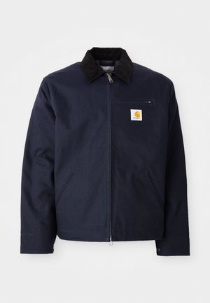 Navy blue jacket made of canvas with a black corduroy collar, zip closure, front pocket, and logo patch on left chest.