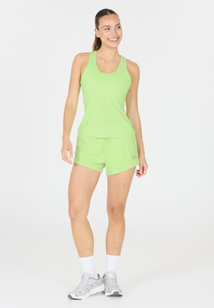 Limegrön träningslinne och matchande shorts. Shortsen har dragsko och en något rundad nederkant. Bärs med grå träningsskor och vita strumpor.