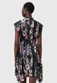 Blumenkleid mit schwarzem Hintergrund, transparentem Material, gerafften Cap-Ärmeln und geschichtetem Saum. Verfügt über einen Reißverschluss auf der rückseitigen Seite und vertikale Streifendetails.