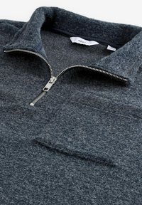 Pull en polaire gris avec col à demi-zip, présentant une texture douce, une poche poitrine et des éléments en métal argenté pour la fermeture.