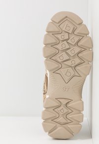 Semelle de chaussure beige avec des rainures profondes, des motifs géométriques et le numéro "37" indiquant la taille sur un fond blanc uni.