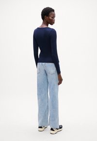 Tricou cu mânecă lungă de culoare bleumarin, asortat cu blugi evazați de culoare albastru deschis. Textură netedă cu un design ușor striat. Încălțămintea prezintă accente negre și crem.