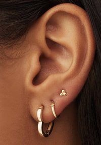 Gold Hoop-Ohrringe mit wellenförmigem Design und einem kleinen goldenen Stecker, der mit drei runden Akzenten verziert ist, präsentiert an einem Ohr mit dunklem Haar.