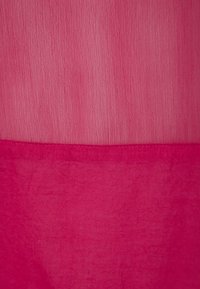 Fuksjowa tkanina o pomarszczonej fakturze, z gładką i płaską dolną sekcją. Ogólny wzór jest jednolity i monochromatyczny.