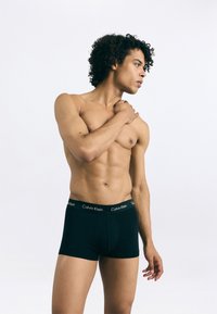Boxeri scurți negri Calvin Klein, cu un elastic moale la talie, având textul cu logo-ul brandului. Modelul pozează pe un fundal neutru, evidențiind croiala și designul.