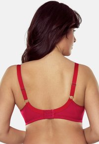 Red bra with adjustable straps, hook-and-eye closure, smooth texture, and seamless design. Features circular hardware accents.