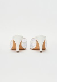 Mules blancos de tacón con un patrón tejido texturizado, adornados con strass transparentes. Plantilla de color marrón claro con un elegante tacón blanco y puntera marrón.