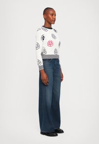 Hvit strikkegenser med rose mønster, med en rød rose, parret med vide mørkeblå denimjeans og svarte ankelstøvletter.