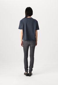 Mørkeblå kortærmet t-shirt med rund hals, lavet af blødt stof, parret med mørkegrå slim-fit jeans og sorte flade sko.
