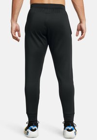 Svarta sportiga joggers med avsmalnande ben, elastisk midja och dragkedjefickor på sidorna. Bärs med flerfärgade sportskor.