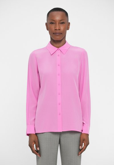 Camisa de manga larga, con botones, en un rosa brillante, hecha de una tela suave, con cuello y mangas abotonadas, combinada con pantalones de rayas grises.