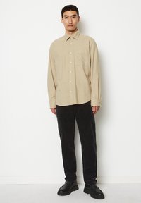 Beige kariertes Langarmhemd mit Knopfverschluss, kombiniert mit schwarzen Cordhosen und schwarzen Schnürschuhen. Einfaches Design und Texturen.