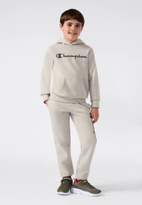 Light gray hoodie and sweatpants set with a front pocket. Features "Champion" logo in dark blue. Sneakers with olive green accents.